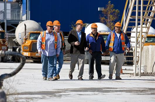 A group of concrete producers walking on a construction site. In the background: four concrete mixer trucks.