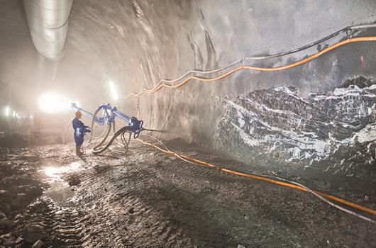 Construction worker spraying of concrete with a machine in a tunnel.